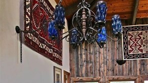 A rustic dining area with a wooden table and chairs, a chandelier, and a view of greenery outside.