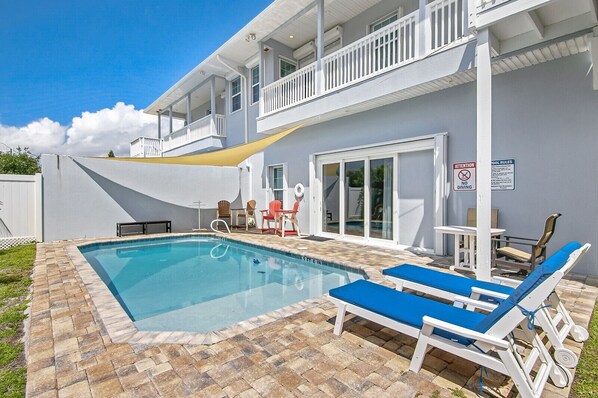 A swimming pool with lounge chairs, a covered patio, and a two-story building with a balcony.