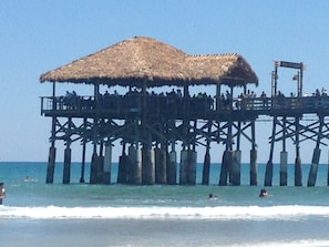 A pier with a thatched roof and multiple levels, extending into the sea.