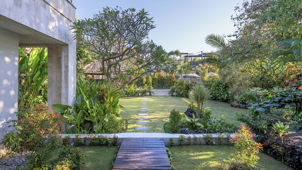 A garden pathway leading to a building with a modern design, surrounded by lush greenery and various plants. - The ultimate Bali beachside getaway at Villa Kaira Estate, a 7-bedroom luxury villa in Berawa, Canggu. The Estate offers daily breakfast, a full-time private chef, airport transfers, complimentary massages, housekeeping, and a dedicated driver. (North Kuta)