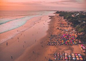 A beach with people and colorful umbrellas, a clear sky, and a sunset.