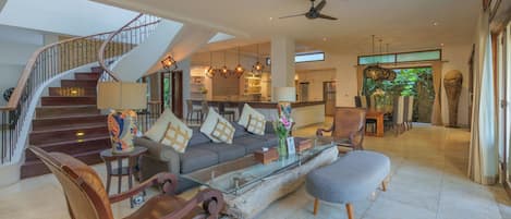 A spacious living area with a staircase, modern furniture, and a large window offering a view of the outdoors.