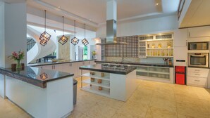 A modern kitchen with a central island, built-in appliances, and pendant lighting. - The ultimate Bali beachside getaway at Villa Kaira Estate, a 7-bedroom luxury villa in Berawa, Canggu. The Estate offers daily breakfast, a full-time private chef, airport transfers, complimentary massages, housekeeping, and a dedicated driver. (North Kuta)