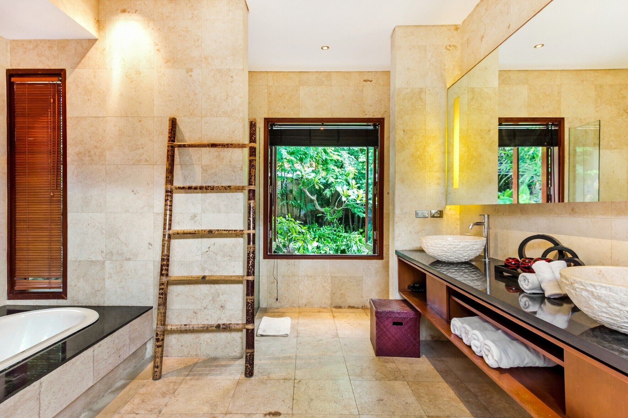 Une salle de bain moderne avec une baignoire, un grand miroir, un lavabo avec un vasque sur pied, une échelle et une fenêtre donnant sur un paysage verdoyant.