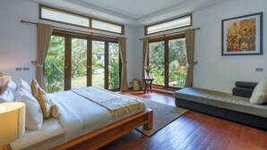 A spacious bedroom with a large bed, a sofa, and a view of a garden through large windows. - The ultimate Bali beachside getaway at Villa Kaira Estate, a 7-bedroom luxury villa in Berawa, Canggu. The Estate offers daily breakfast, a full-time private chef, airport transfers, complimentary massages, housekeeping, and a dedicated driver. (North Kuta)