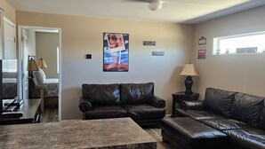 A living room with a dark leather sofa, a coffee table, and a kitchen area with a countertop. - Movie House (Thompson)