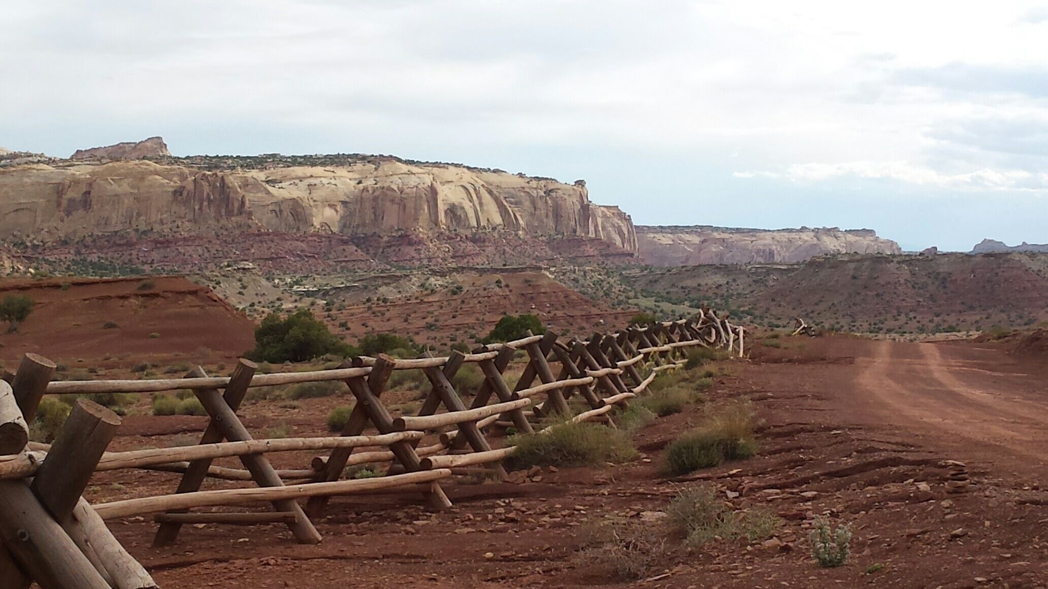 A rugged landscape with a dirt road, a wooden fence, and a large rock formation in the background.