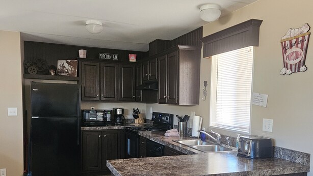 A kitchen with dark wooden cabinets, a stainless steel refrigerator, a microwave, a stove, and a sink. - Movie House (Thompson)