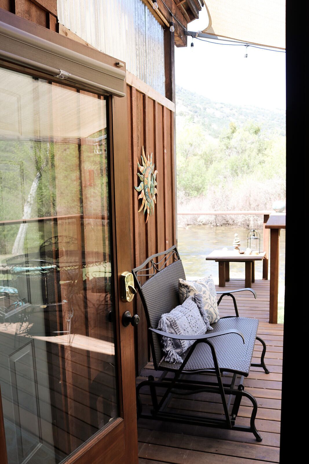 A wooden deck with a metal-framed chair and a small table, overlooking a river.
