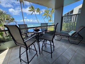 A balcony with a table and chairs, overlooking a beach and palm trees. - Absolutely Beachfront -- Hale Mahina Beach Resort -- B206 (Napili-Honokowai)