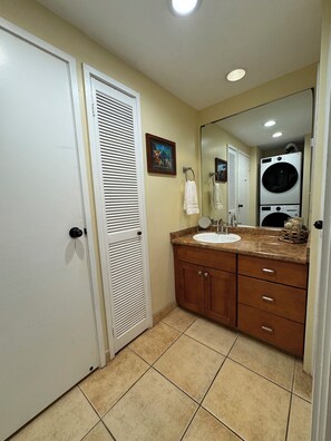 A bathroom with a sink, mirror, and stacked washer and dryer. - Absolutely Beachfront -- Hale Mahina Beach Resort -- B206 (Napili-Honokowai)