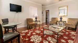 A living room with a TV, two patterned armchairs, a glass coffee table, a red floral rug, and a ceiling fan. - Walk to all the French Quarter attractions.  A great space to enjoy NOLA (New Orleans)