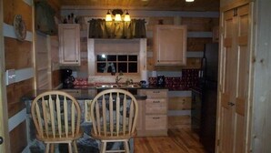 A cozy cabin-style kitchen with wooden walls, a stone accent wall, two wooden bar stools, a built-in sink, and a refrigerator. - Your Mayberry Get-a-Way Cabin- Only 6 miles from Downtown Mount Airy (Mount Airy)