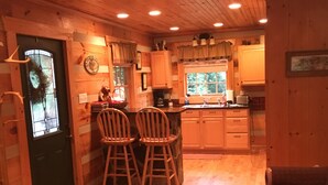 A cozy cabin interior with a wooden interior, a bar area with stools, a dining table, and a fireplace. - Your Mayberry Get-a-Way Cabin- Only 6 miles from Downtown Mount Airy (Mount Airy)