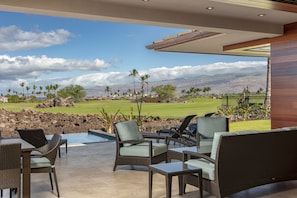 Un espace aménagé au bord de la piscine, avec des meubles en osier et une vue sur un terrain de golf et des montagnes.