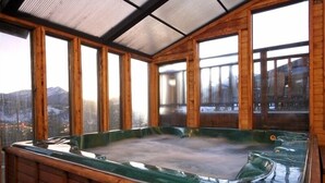 Un jacuzzi con paredes de madera y ventanas amplias que ofrecen vistas a la montaña.