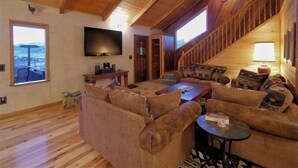 Una sala de estar acogedora con piso de madera, un televisor grande y una escalera que conduce a un nivel superior.