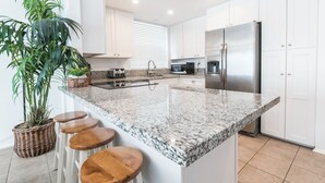 A modern kitchen with white cabinets, a stainless steel refrigerator, a granite countertop, and a potted plant.