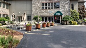 Ein Steinhaus mit einem Schild, das '19th HOLE BAR and GRILL' zeigt, Außenbereich mit Sitzgelegenheiten und amerikanischen Flaggen sowie ein Parkplatz.
