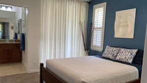 A bedroom with a bed, a nightstand, a mirror, a window with blinds, a wall-mounted artwork, and a bathroom visible in the background. - Beautifully Furnished-Great for families 3 Bed, 2 1/2 Bath Nihilani, Princeville (Princeville)