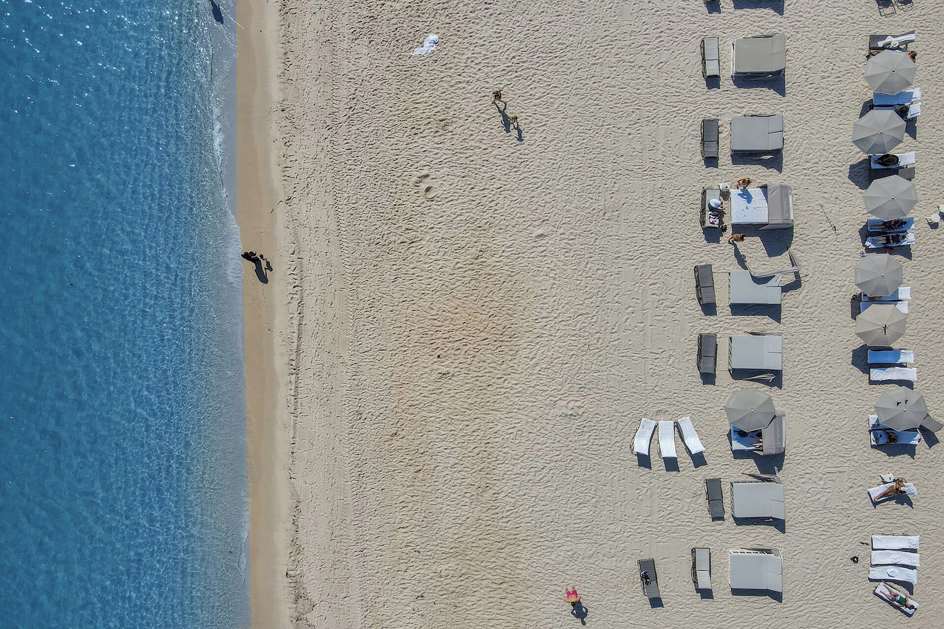 Vista aérea de una playa con hileras de tiendas de campaña y sombrillas, arena dorada y un mar tranquilo.