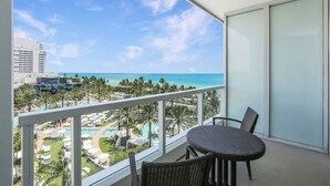 A balcony with a view of a resort pool, palm trees, and a beach.