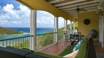 A covered outdoor seating area with a view of the ocean, a grill, and a dining table with chairs.