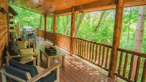 A wooden deck with outdoor furniture, a grill, and a view of a forest.
