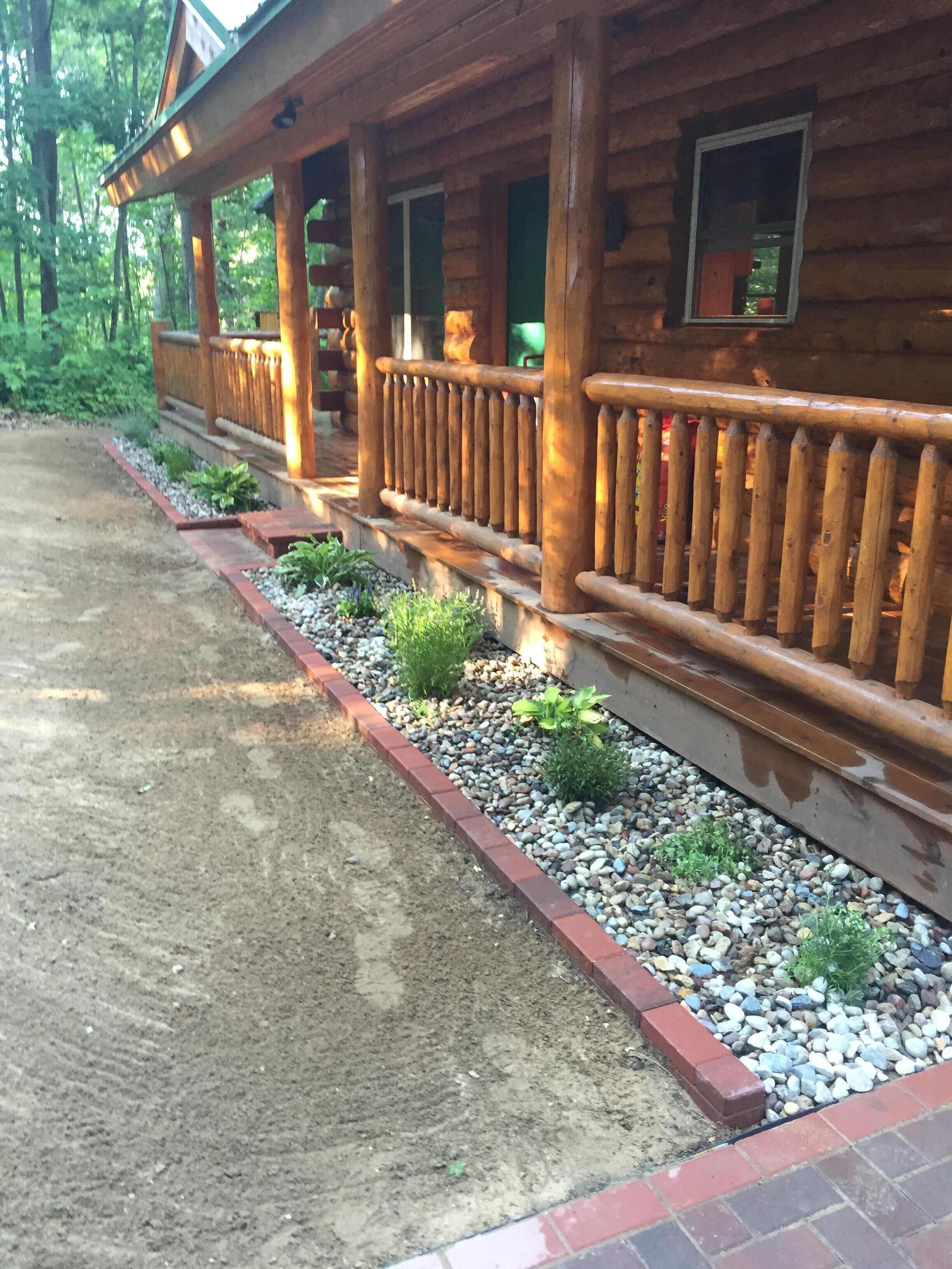 A wooden cabin with a porch, a gravel pathway, and a small garden area with plants and pebbles.