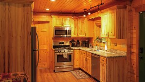 A wooden cabin interior with a kitchen featuring a stove, oven, microwave, and sink.