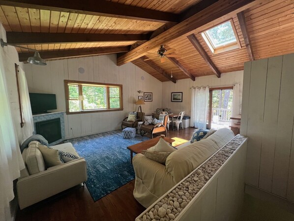 A spacious living room with a fireplace, a sofa, a dining table, and a ceiling fan. - Bright and Spacious Cape House with Central Air (Wellfleet)