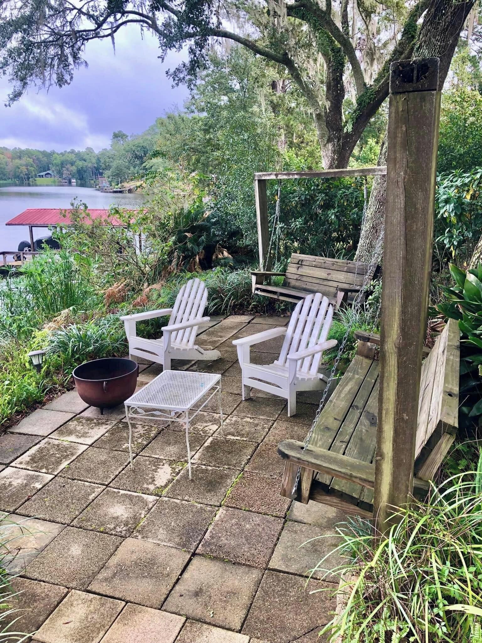Une terrasse avec des fauteuils Adirondack blancs, une table en métal et une balançoire en bois.