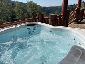 A hot tub on a wooden deck with a forest view.