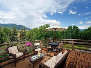 Eine Terrasse mit Korbmöbeln, einem Tisch und Stühlen mit Blick auf eine gebirgige Landschaft.