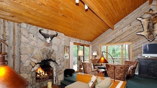 A cozy cabin interior with a stone fireplace, wooden ceiling, and a comfortable seating area.