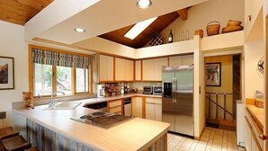 A modern kitchen with a central island, built-in appliances, and a wooden ceiling.