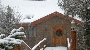 A snow-covered wooden staircase leading to a house with a red door and a wreath.