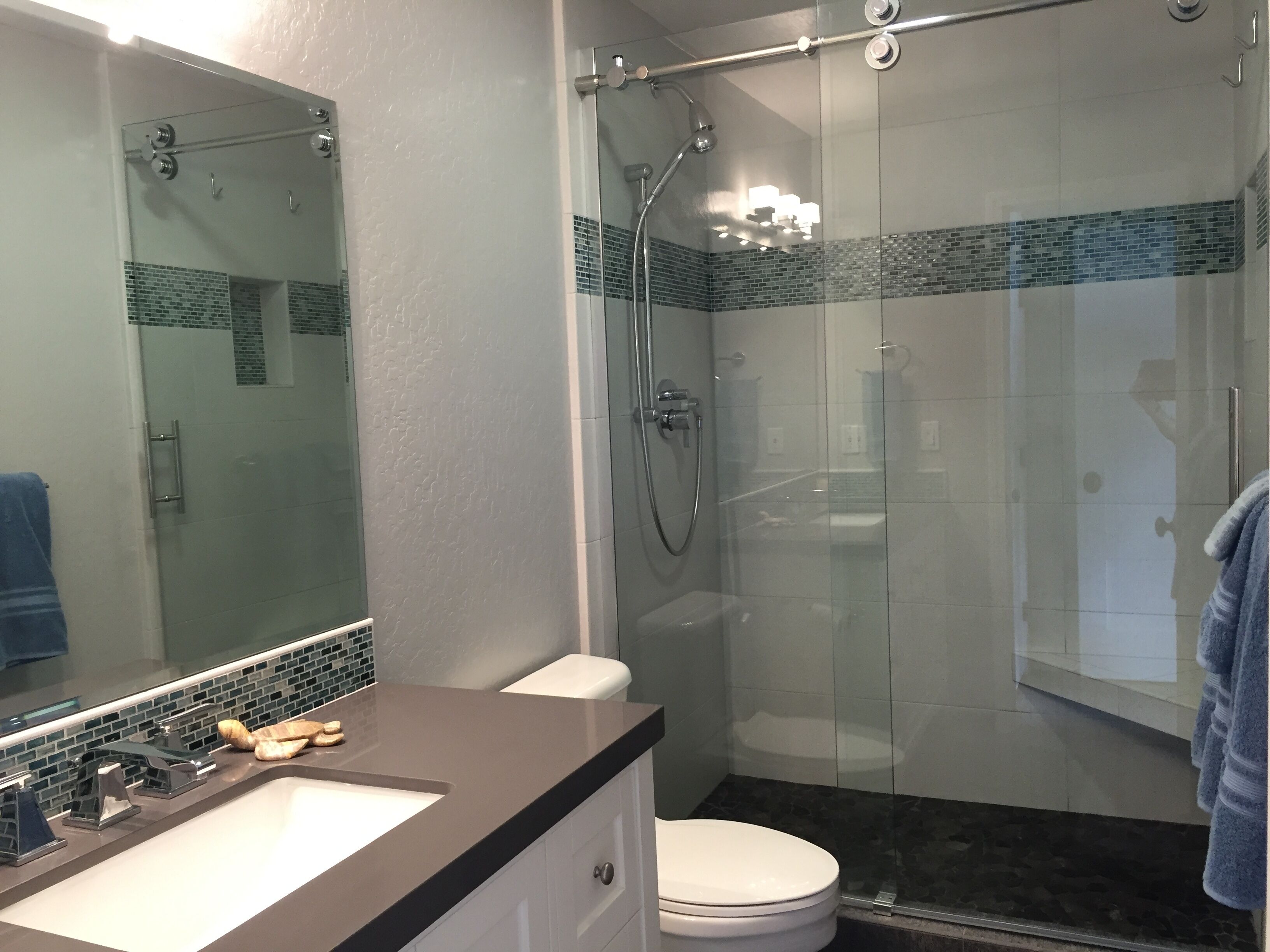 Un baño moderno con ducha envuelta en vidrio, inodoro blanco y tocador con lavamanos y espejo.