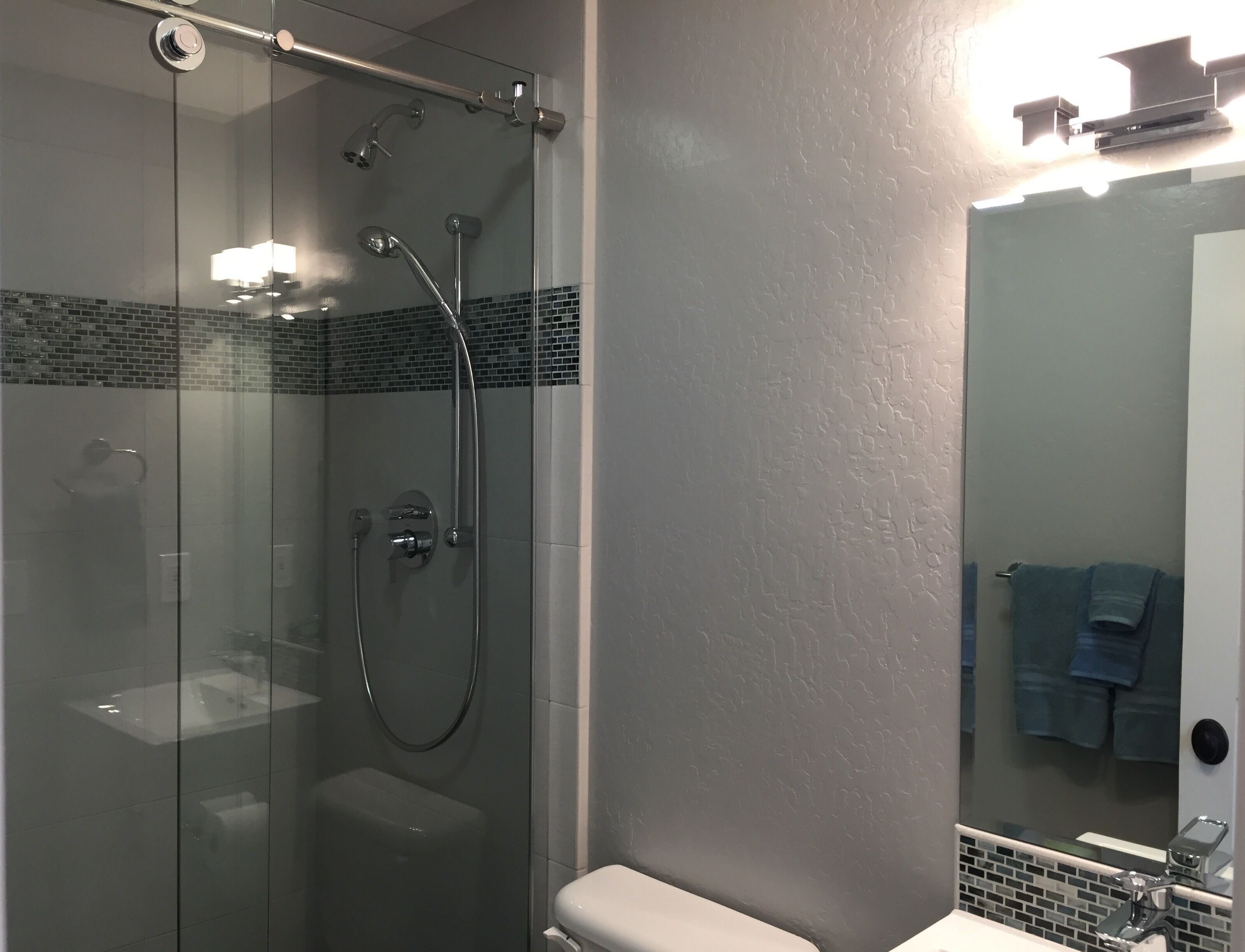 Ein modernes Badezimmer mit einer gläsernen Duschkabine, einer Toilette und einem Waschbecken mit Spiegel.