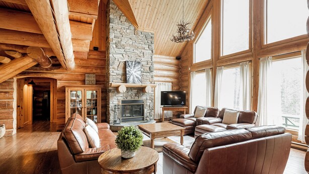 A log cabin interior with a stone fireplace, leather sofas, and large windows. - ChaletsOais Luxury lakefront 5 bedroom log home with private hot tub  (Mille-Isles)