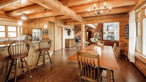 A wooden interior with a dining area, kitchen, and a stone fireplace. - ChaletsOais Luxury lakefront 5 bedroom log home with private hot tub  (Mille-Isles)