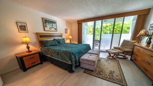 Ein Schlafzimmer mit Bett, Nachttischen, einem Sessel, einer Kommode und Blick auf Grün durch das Fenster.