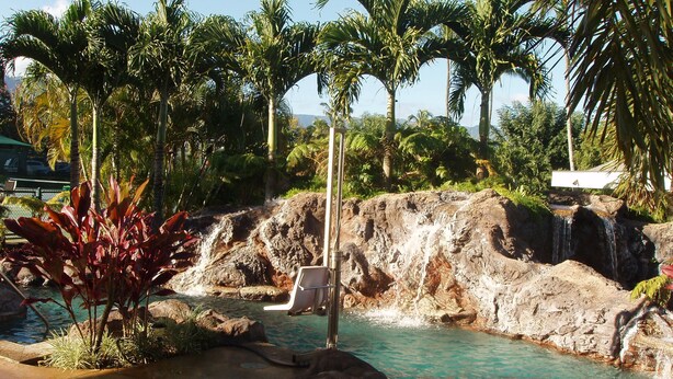 Ein Poolbereich mit Wasserfall, umgeben von Palmen und Felsen.