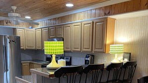 Una cocina con gabinetes de madera, un refrigerador de acero inoxidable, una lámpara amarilla y una zona de comedor con cuatro sillas.