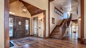 A spacious hallway with wooden floors, a staircase, and a large wooden door.