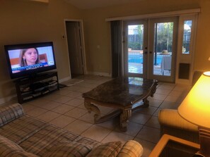 Een woonkamer met een televisie, een bank, een salontafel en een schuifdeur naar een buitenruimte.