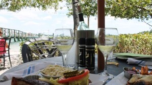 Een tafel met een maaltijd bestaande uit een sandwich, een salade en een bijgerecht, samen met twee glazen witte wijn en een fles olijfolie.