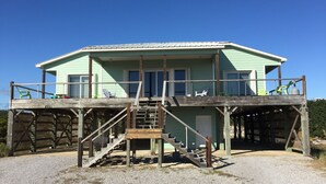 A two-story beach house with a wooden deck, a staircase, and a door. - Family Friendly, Ft Morgan Beach House (Gulf Shores)