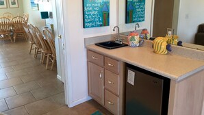 A kitchen with a sink, cabinets, and decorative fish-shaped containers. There are wooden chairs and a dining table in the adjacent room. - Family Friendly, Ft Morgan Beach House (Gulf Shores)