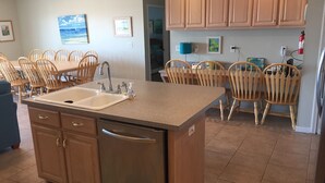 A kitchen with a central island, wooden chairs, a dishwasher, and a refrigerator. - Family Friendly, Ft Morgan Beach House (Gulf Shores)